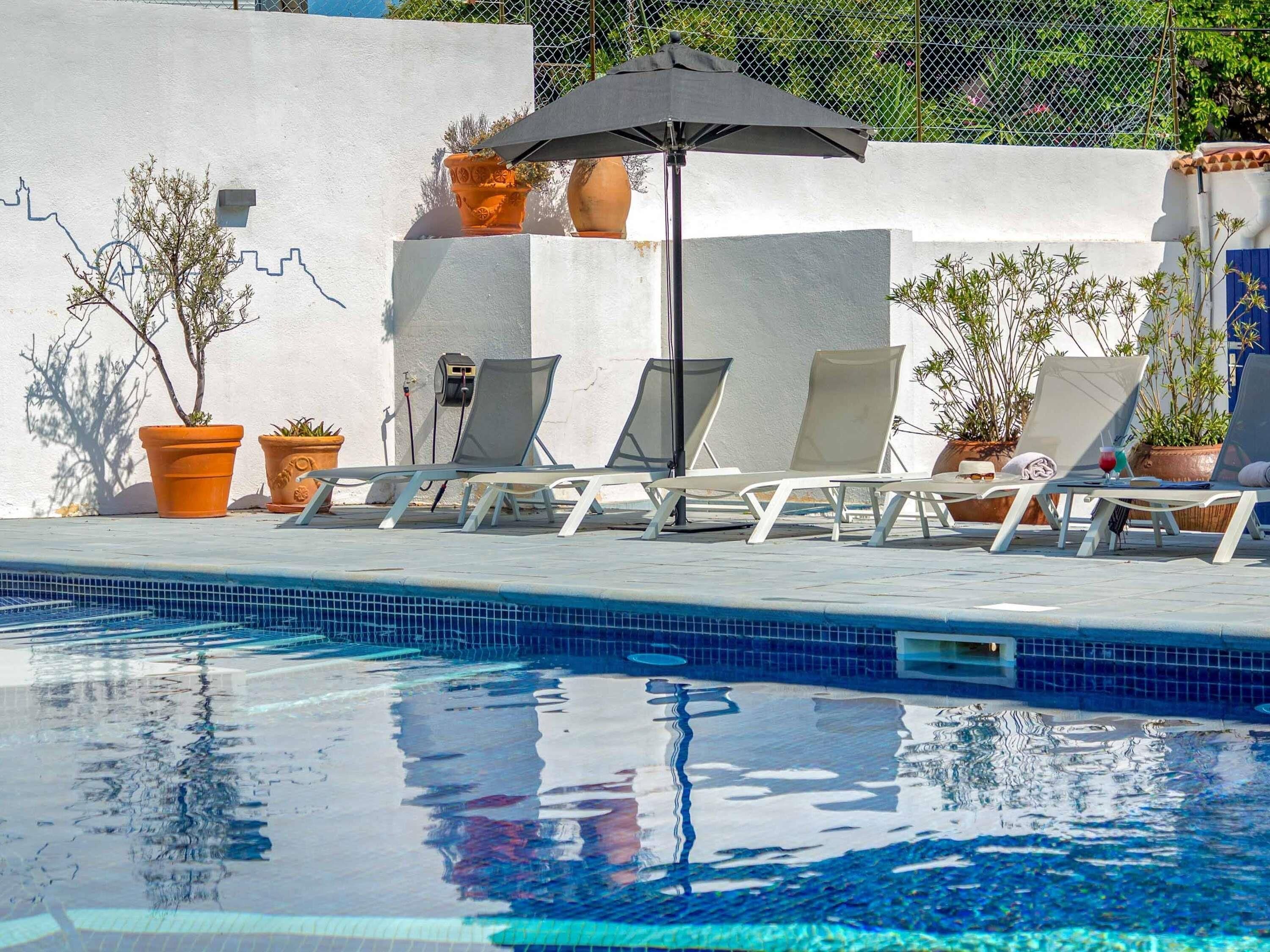 A poolside area with lounge chairs, a pool, and potted plants.