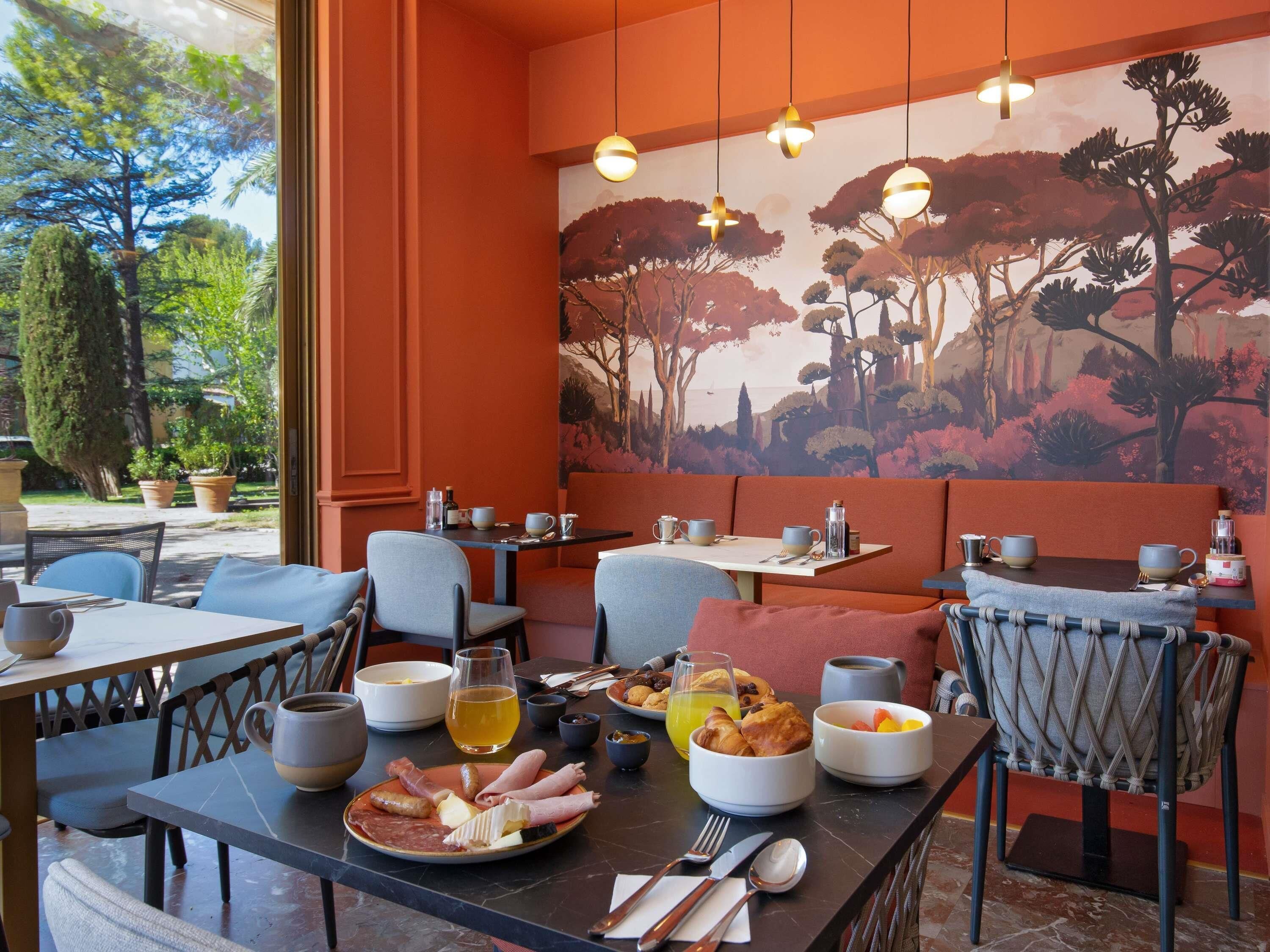 A dining area with tables, chairs, and a mural of trees.