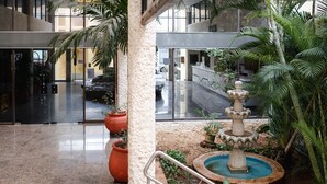 Um átrio interno com uma fonte central, plantas em vasos e uma área de recepção moderna.