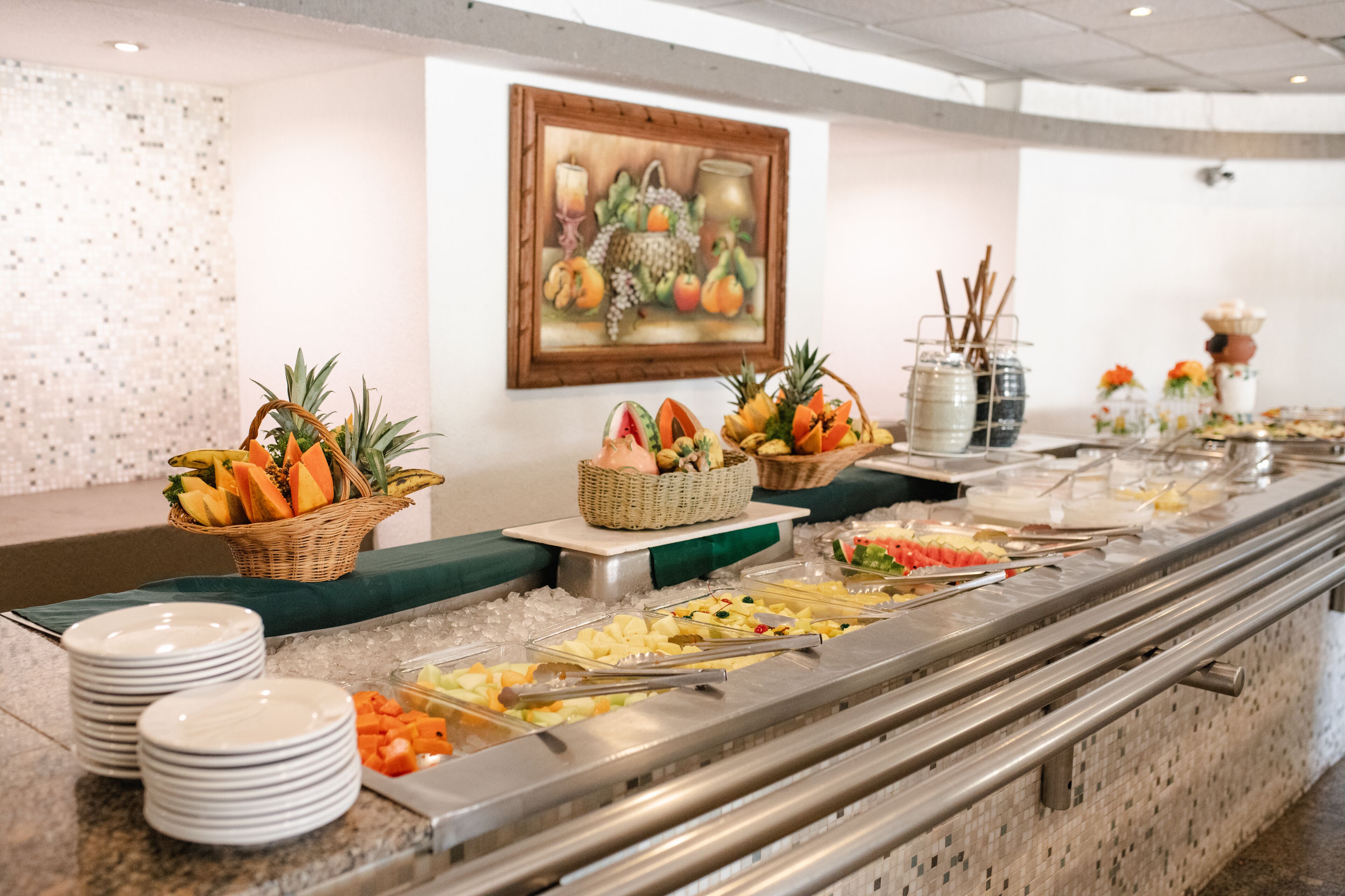 A buffet with various fruits and vegetables, a painting on the wall, and a tiled backsplash.