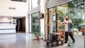 Um hall de hotel com mesa de recepção, carrinho de bagagem e planta em vaso.