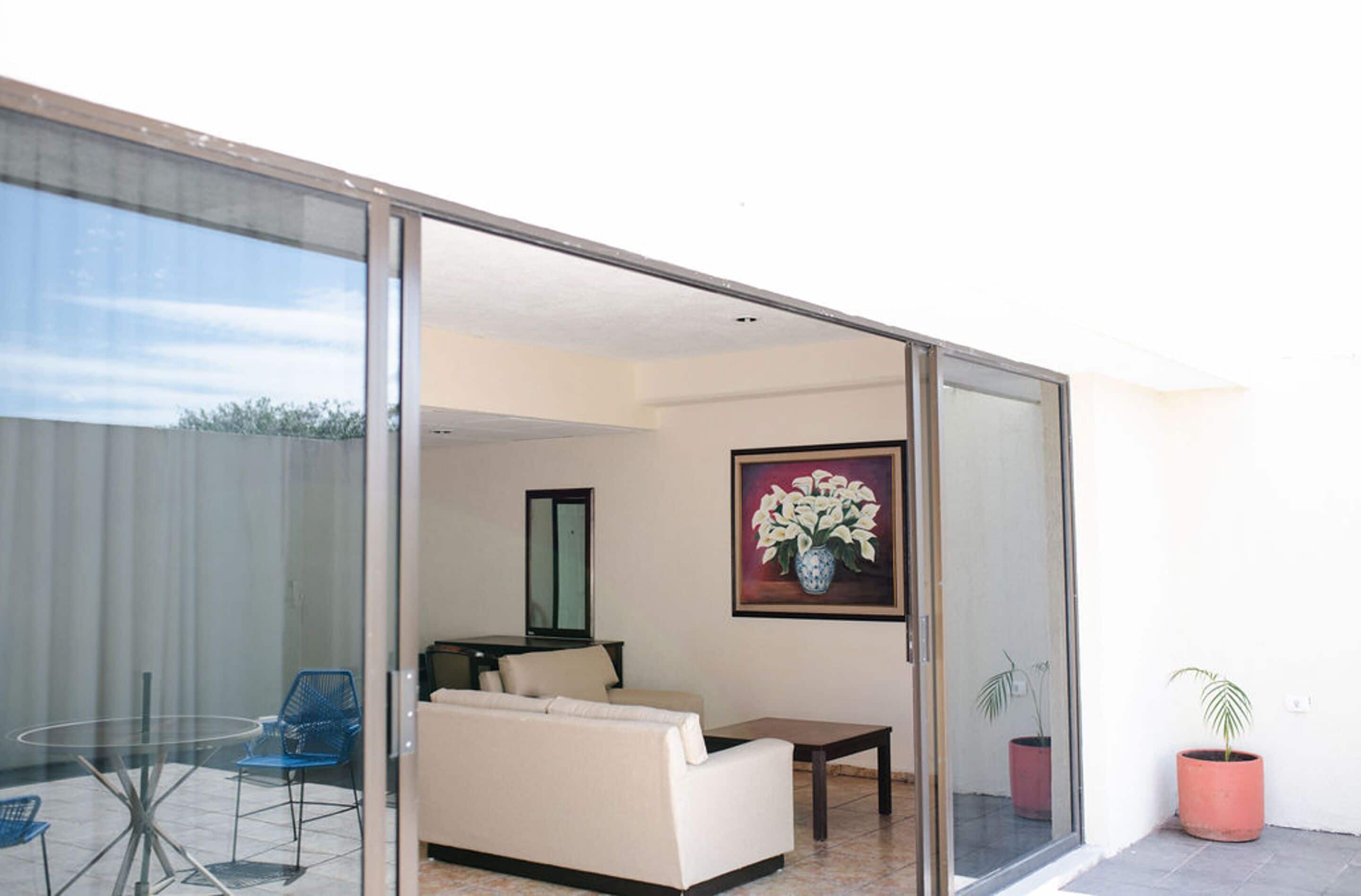A modern living room with a glass door leading to a balcony, a sofa, a coffee table, and a painting of flowers.