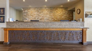 A reception area with a stone wall, a wooden counter, and a decorative panel. - Best Western Plus A Wayfarer's Inn And Suites (Kingman)