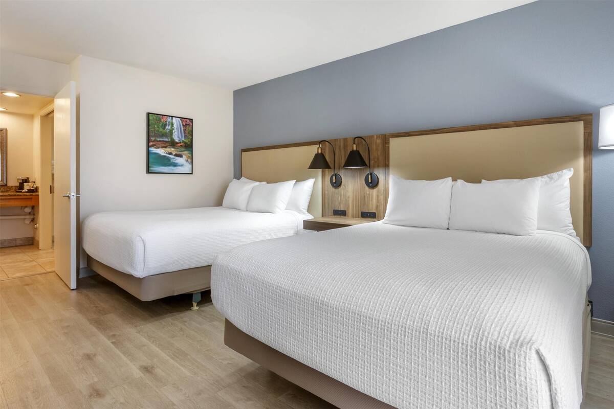 A hotel room with two beds, a painting of a waterfall, and a wooden headboard.