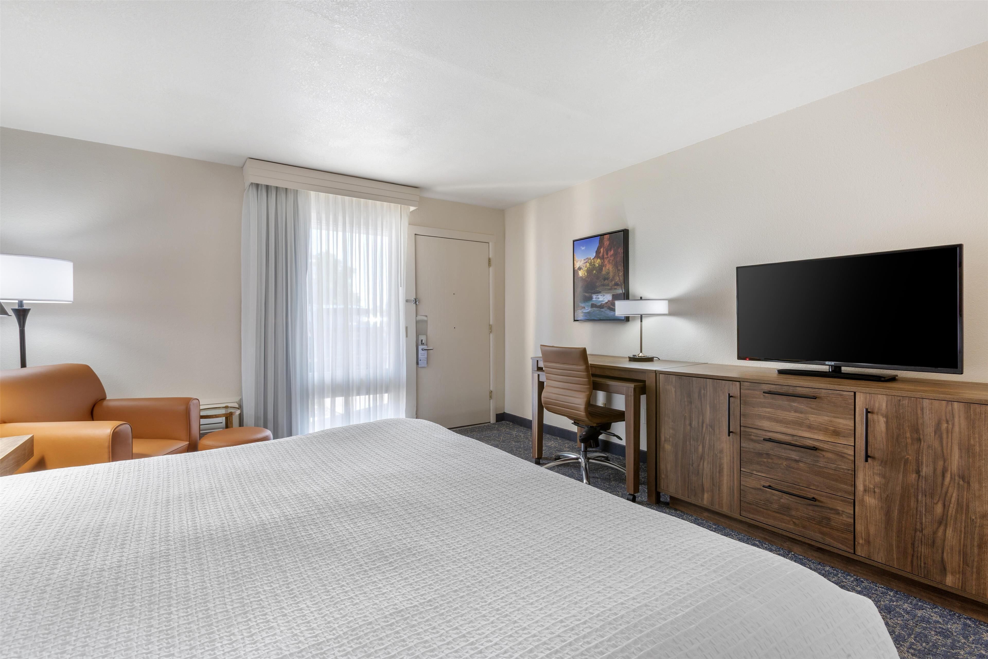 A hotel room with a large bed, a desk with a chair, a television, and a window with curtains.