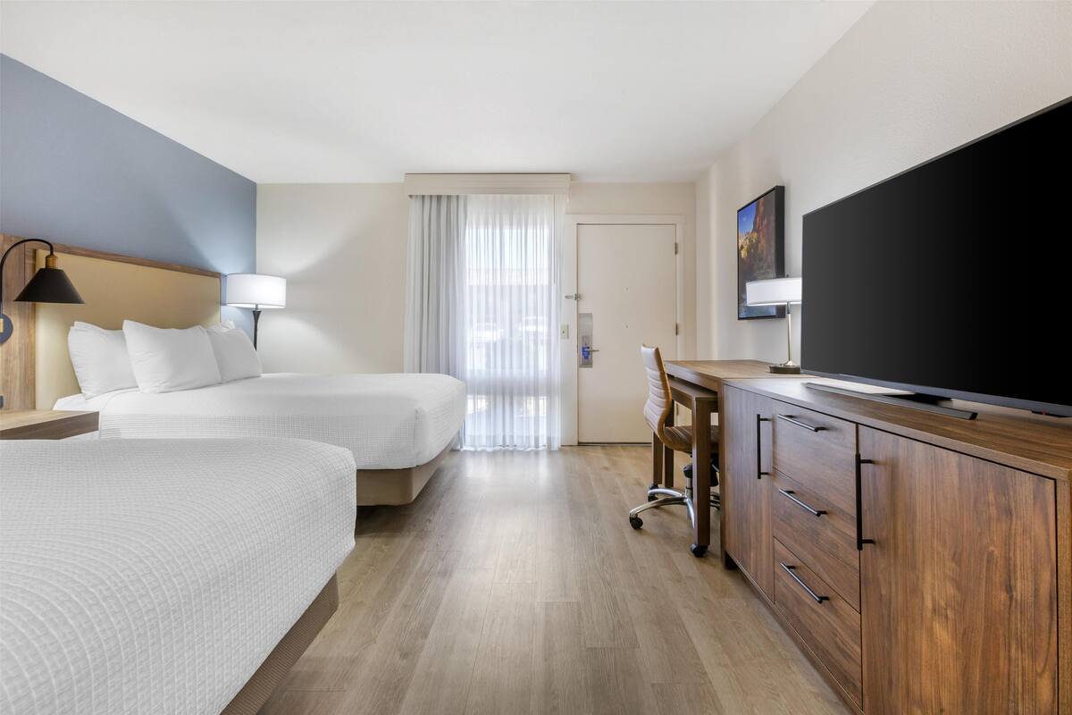 A hotel room with two beds, a desk, a television, and a door leading to the bathroom.