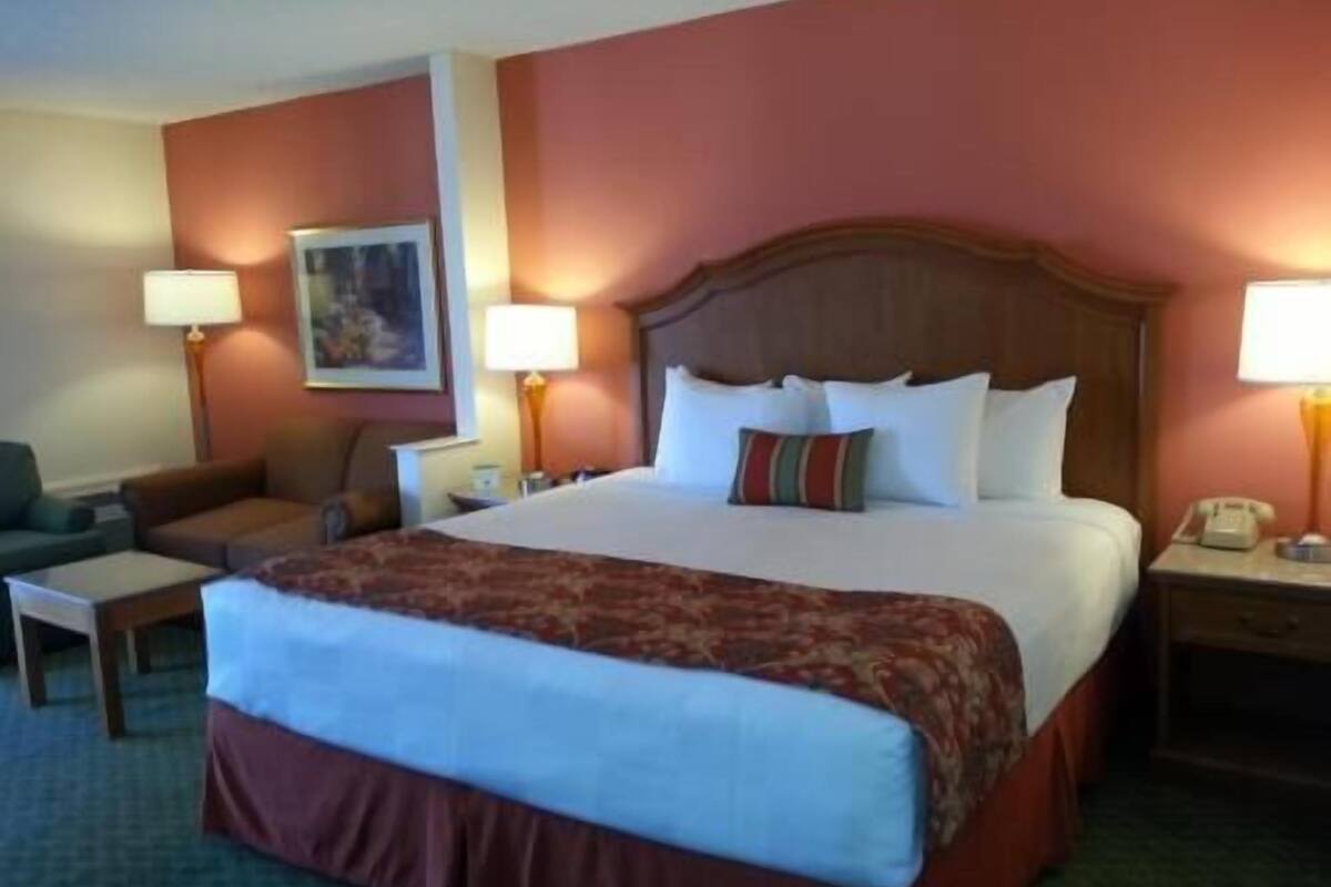 A hotel room with a large bed, two bedside tables with lamps, a chair, and a painting on the wall.