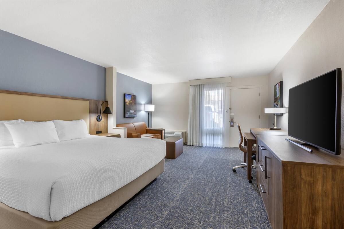 A hotel room with a large bed, a desk, a television, and a window with curtains.