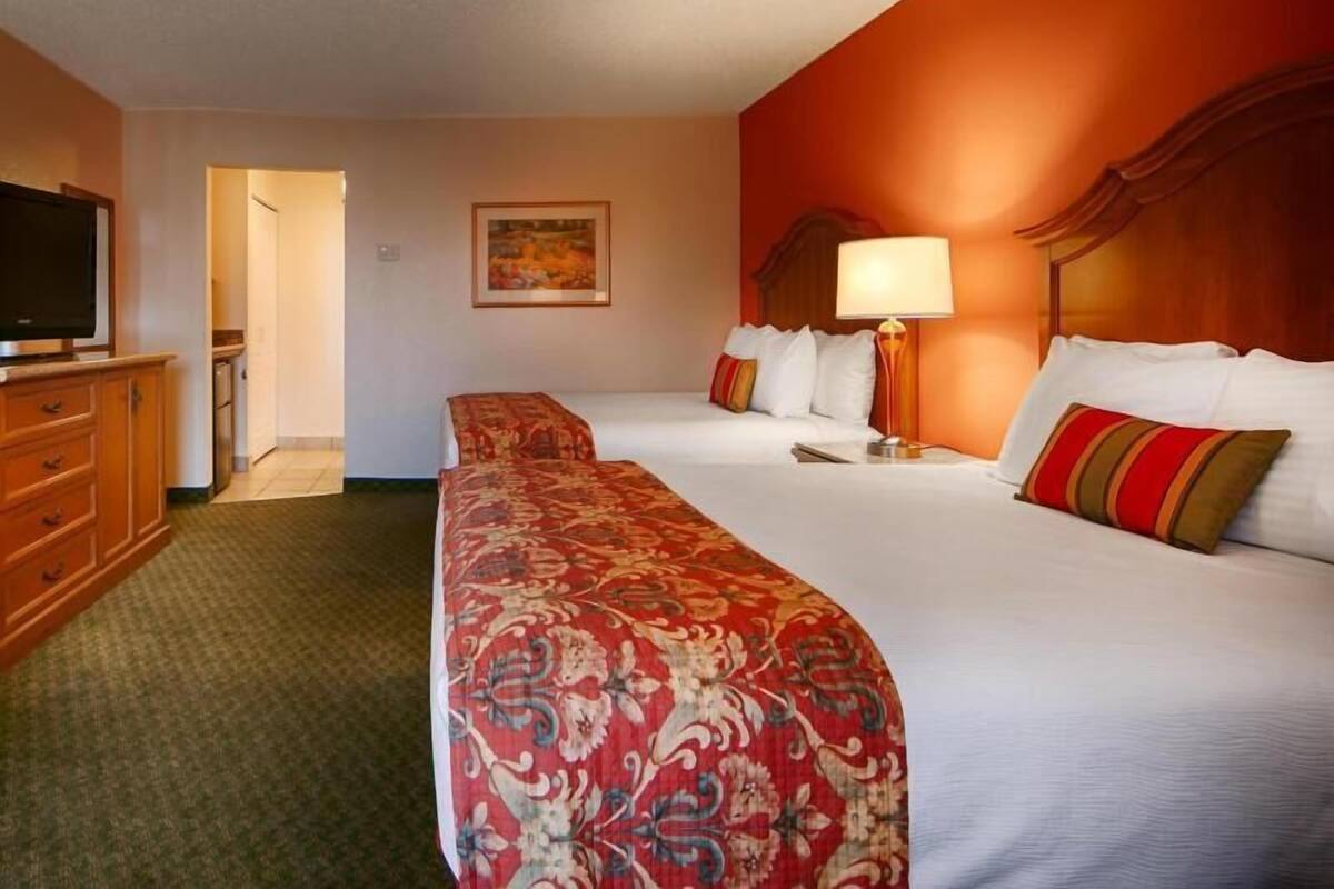 A hotel room with two beds, a television, a desk with a lamp, and a painting on the wall.