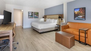 A hotel room with a bed, a desk with a chair, an orange sofa, a small table, and a TV. - Best Western Plus A Wayfarer's Inn And Suites (Kingman)