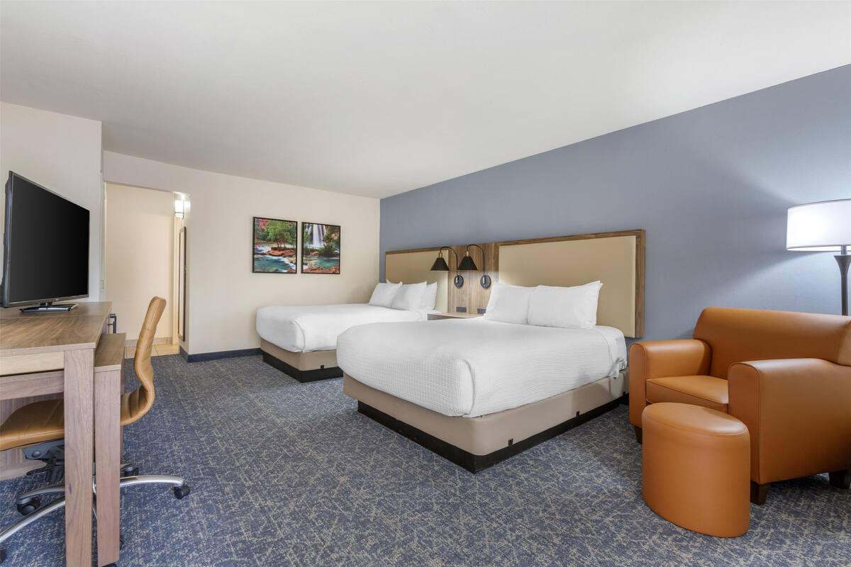 A hotel room with two beds, a desk with a chair, a television, and a lamp.