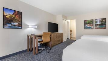A hotel room with a bed, desk, chair, TV, and two framed pictures on the wall.