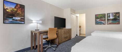 A hotel room with a bed, desk, chair, TV, and two framed pictures on the wall.