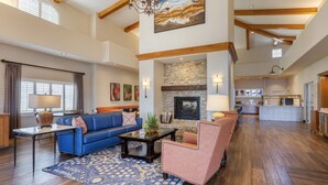 A spacious living room with a fireplace, a blue sofa, a pink armchair, and a wooden floor. - Best Western Plus A Wayfarer's Inn And Suites (Kingman)