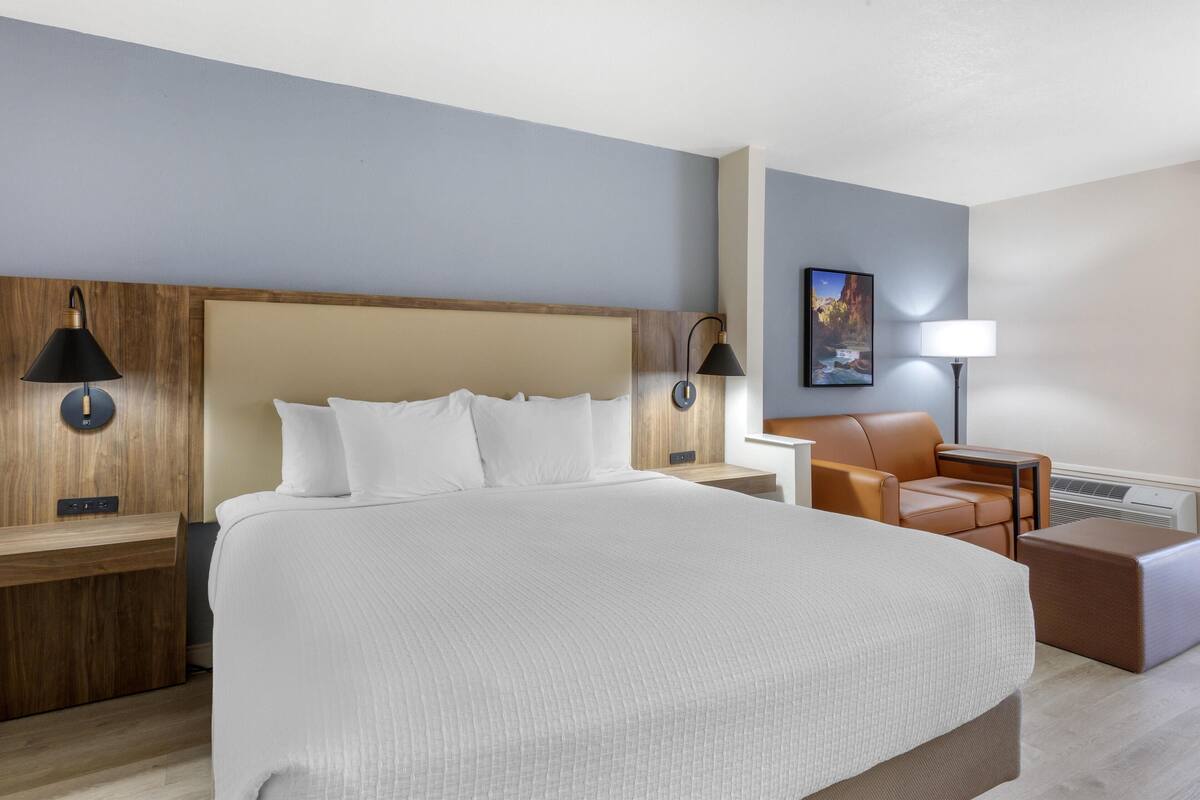 A hotel room with a large bed, two bedside tables with lamps, a brown leather chair, a small table, and a painting on the wall.