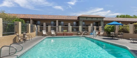 A swimming pool with lounge chairs and umbrellas, surrounded by a building with a tiled roof.