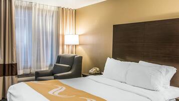 A hotel room with a bed, a chair, a bedside table with a lamp, and a telephone.