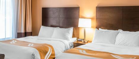 A hotel room with two beds, a nightstand with a lamp, and a view of the outdoors.
