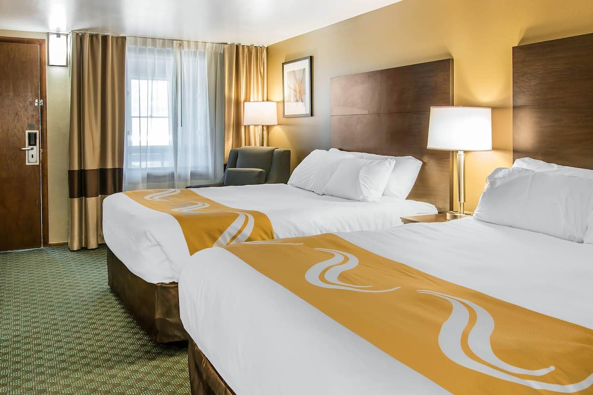 A hotel room with two beds, a desk, a chair, and a window with curtains.