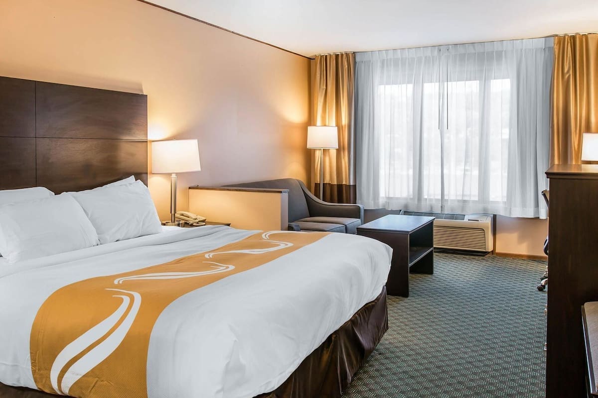 A hotel room with a large bed, a desk, a chair, and a window with curtains.