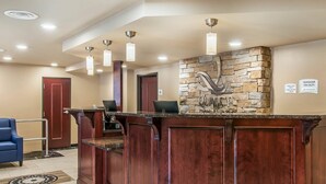 A reception area with a wooden reception desk, a stone accent wall, and a blue chair. - Quality Inn & Suites Houghton Downtown (Houghton)
