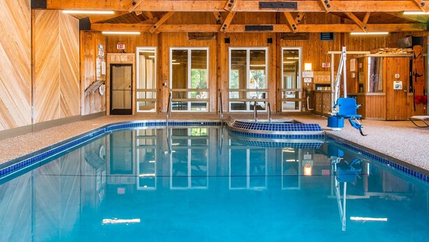 A swimming pool with wooden walls and a tiled floor, surrounded by a wooden deck and a covered area with a blue chair. - Quality Inn & Suites Houghton Downtown (Houghton)