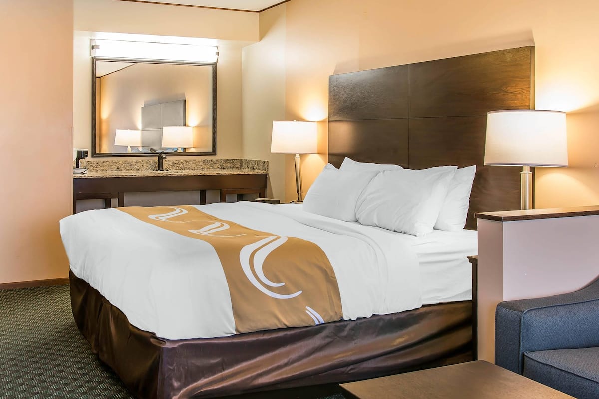 A hotel room with a large bed, a nightstand, a lamp, a mirror, and a bathroom counter.