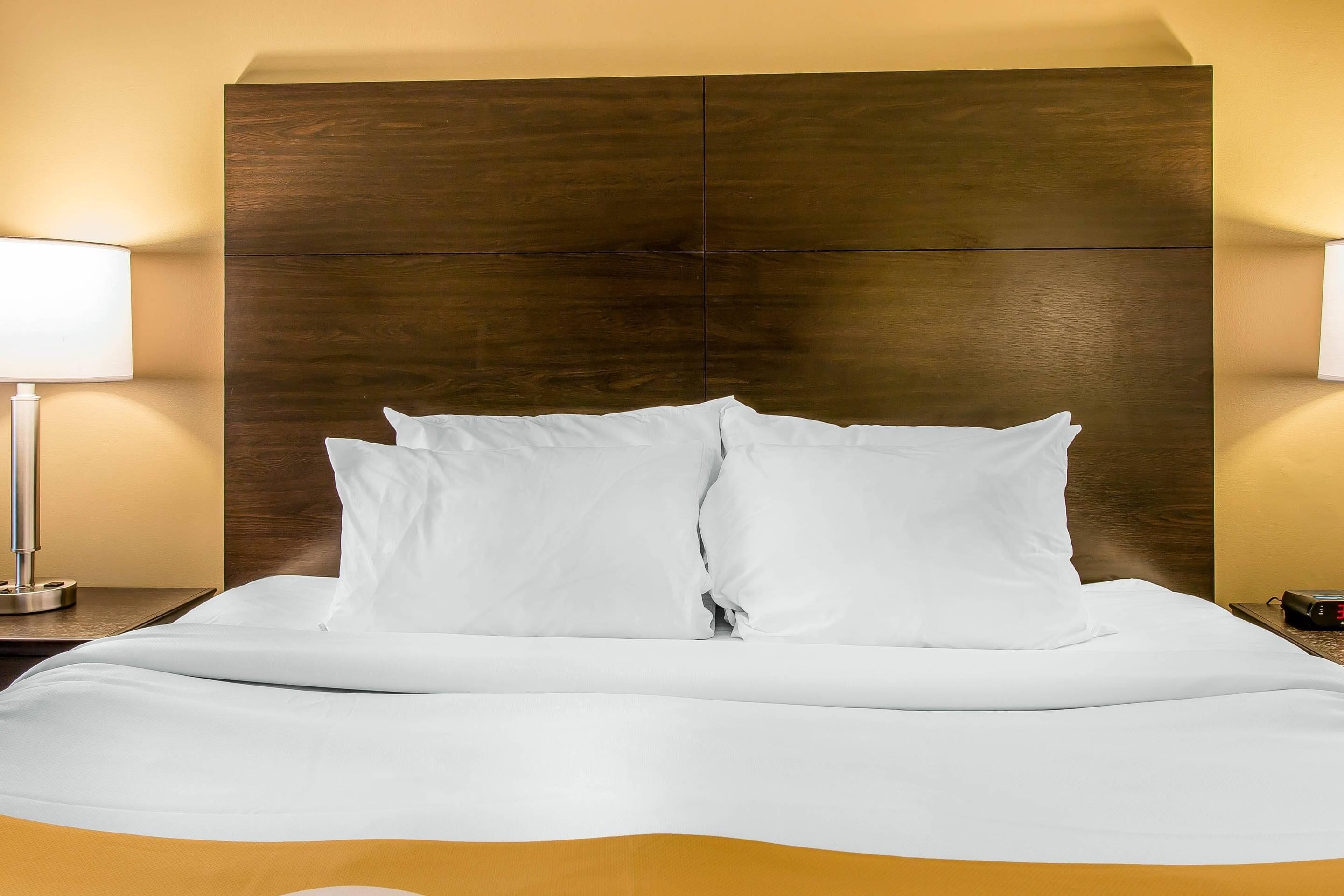 Una cama bien hecha con sábanas y almohadas blancas, un cabecero de madera y dos lámparas de noche.
