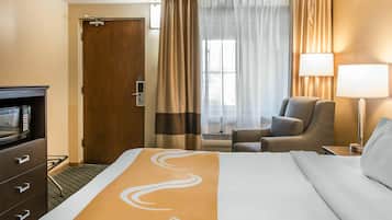 A hotel room with a bed, a chair, a desk, a television, and a door.