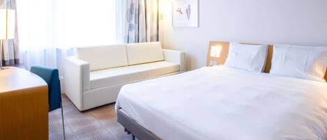 A hotel room with a bed, a sofa, a desk, and a window with curtains.