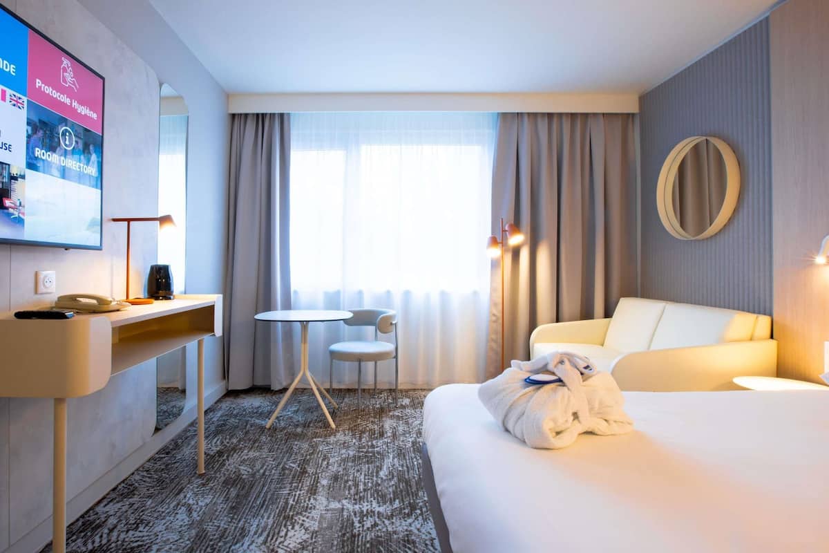 Une chambre d’hôtel équipée d’un lit, d’un bureau, d’une chaise, d’une télévision et d’une fenêtre avec des rideaux.