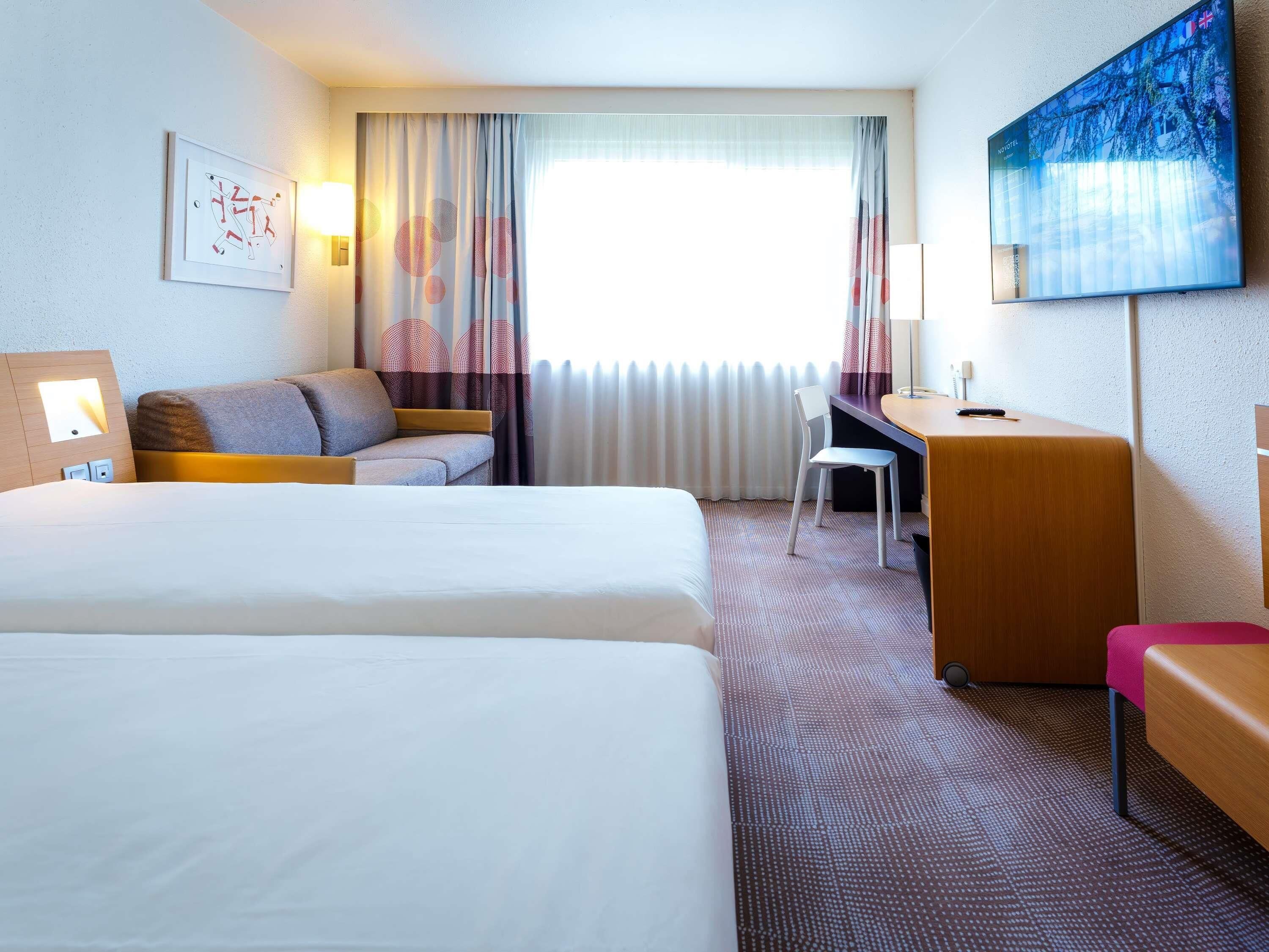 A hotel room with a bed, a sofa, a desk, and a TV.