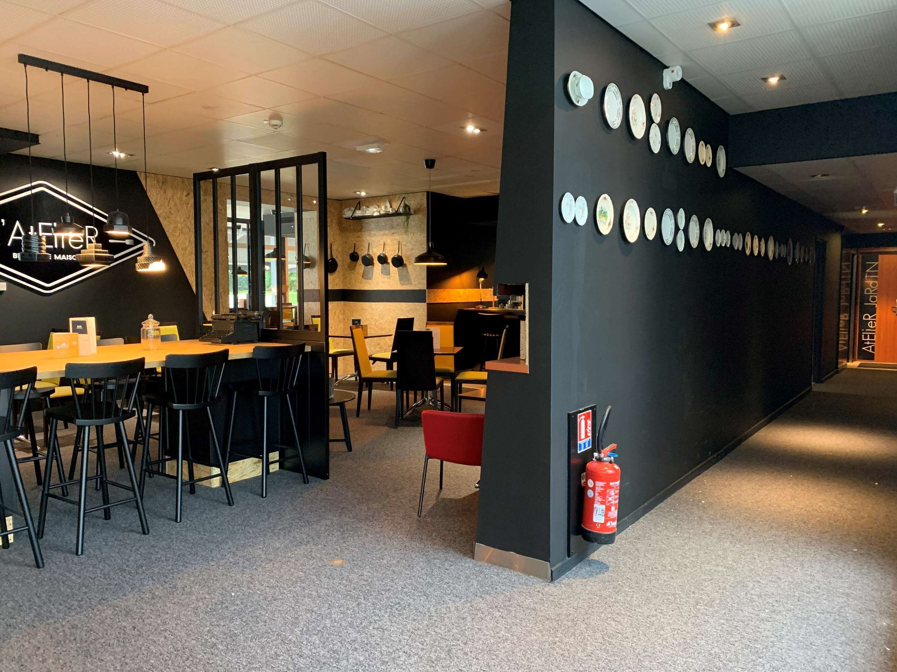 L’intérieur d’un restaurant moderne, aux couleurs noir et blanc, présente un long comptoir avec des chaises, un néon et un extincteur fixé au mur.