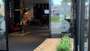 Un espace d’accueil avec une table en bois, une plante en pot et une porte en verre sur laquelle est affiché un panneau « Bienvenue ».