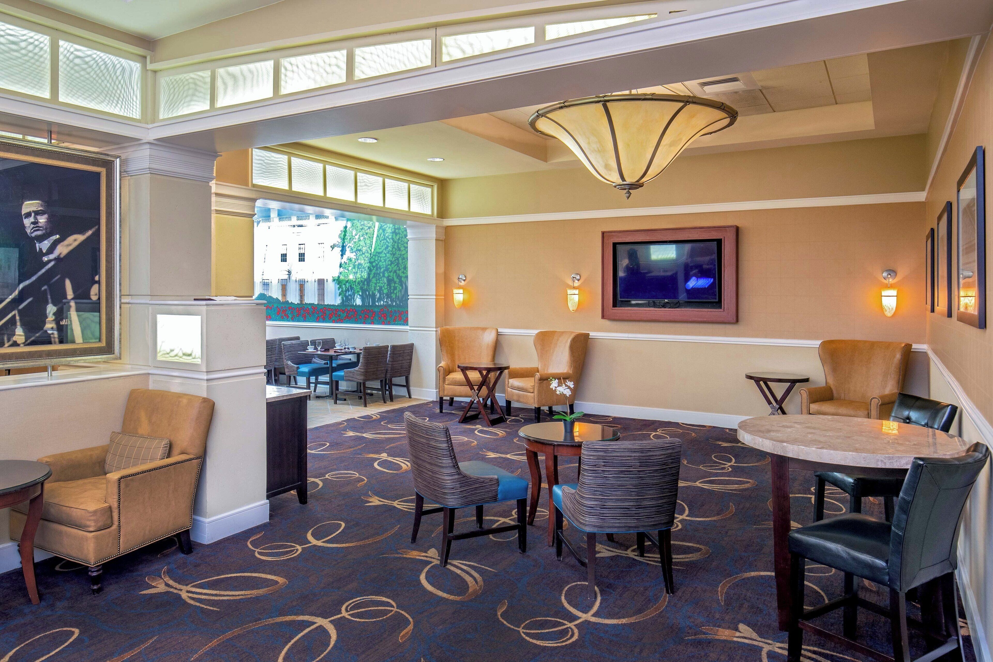 A hotel lobby with a large chandelier, comfortable seating, a television, and a view of the outside.