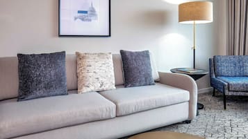 Uma sala de estar moderna com sofá, três almofadas, um abajur, uma mesinha de apoio e uma poltrona azul.