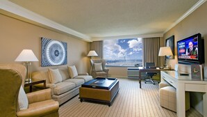 A hotel room with a sofa, armchairs, a coffee table, a desk, a television, and a large window with a city view. - Sheraton Pentagon City Hotel (Arlington)