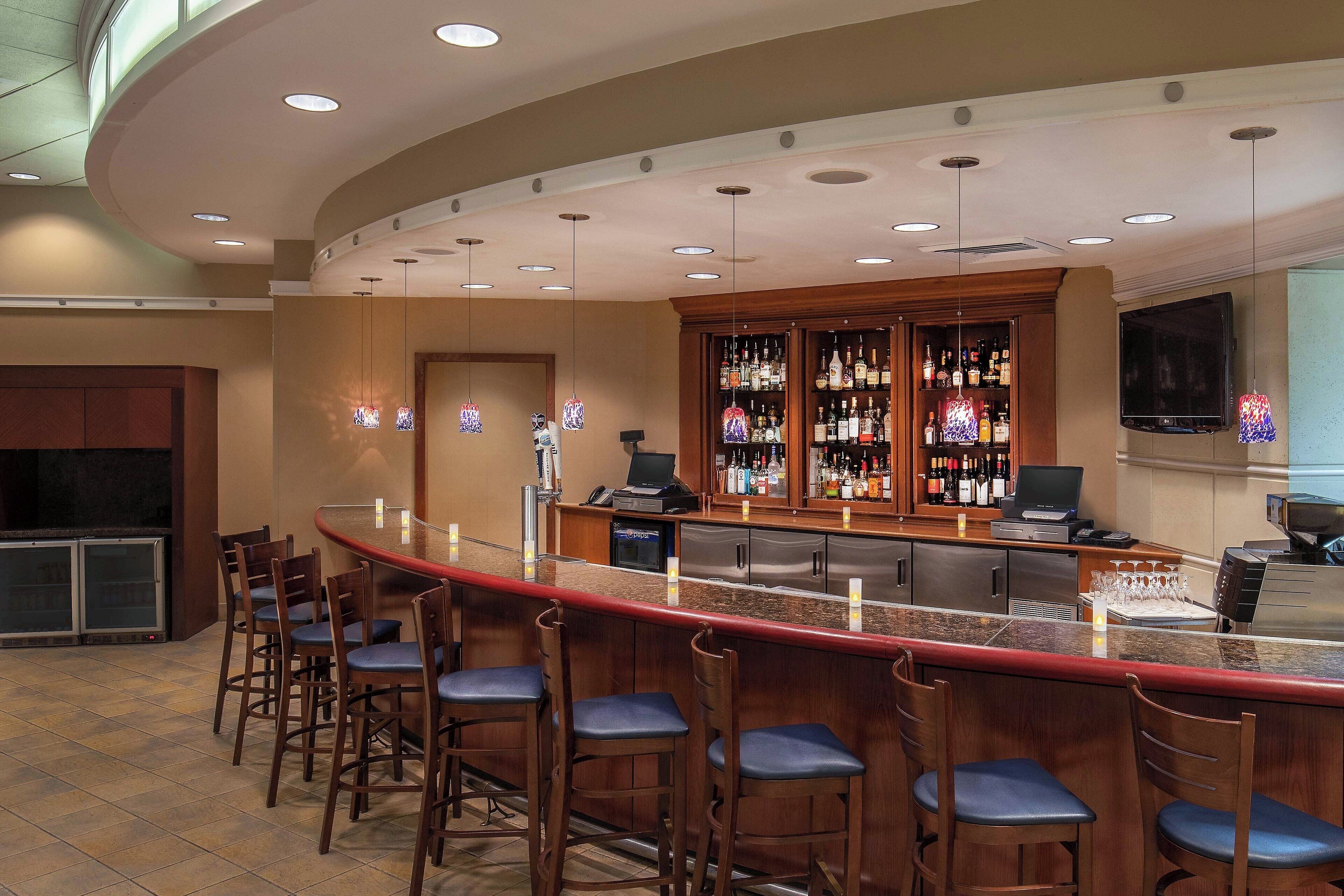 A bar area with a curved counter, multiple stools, a well-stocked liquor cabinet, and a television mounted on the wall.