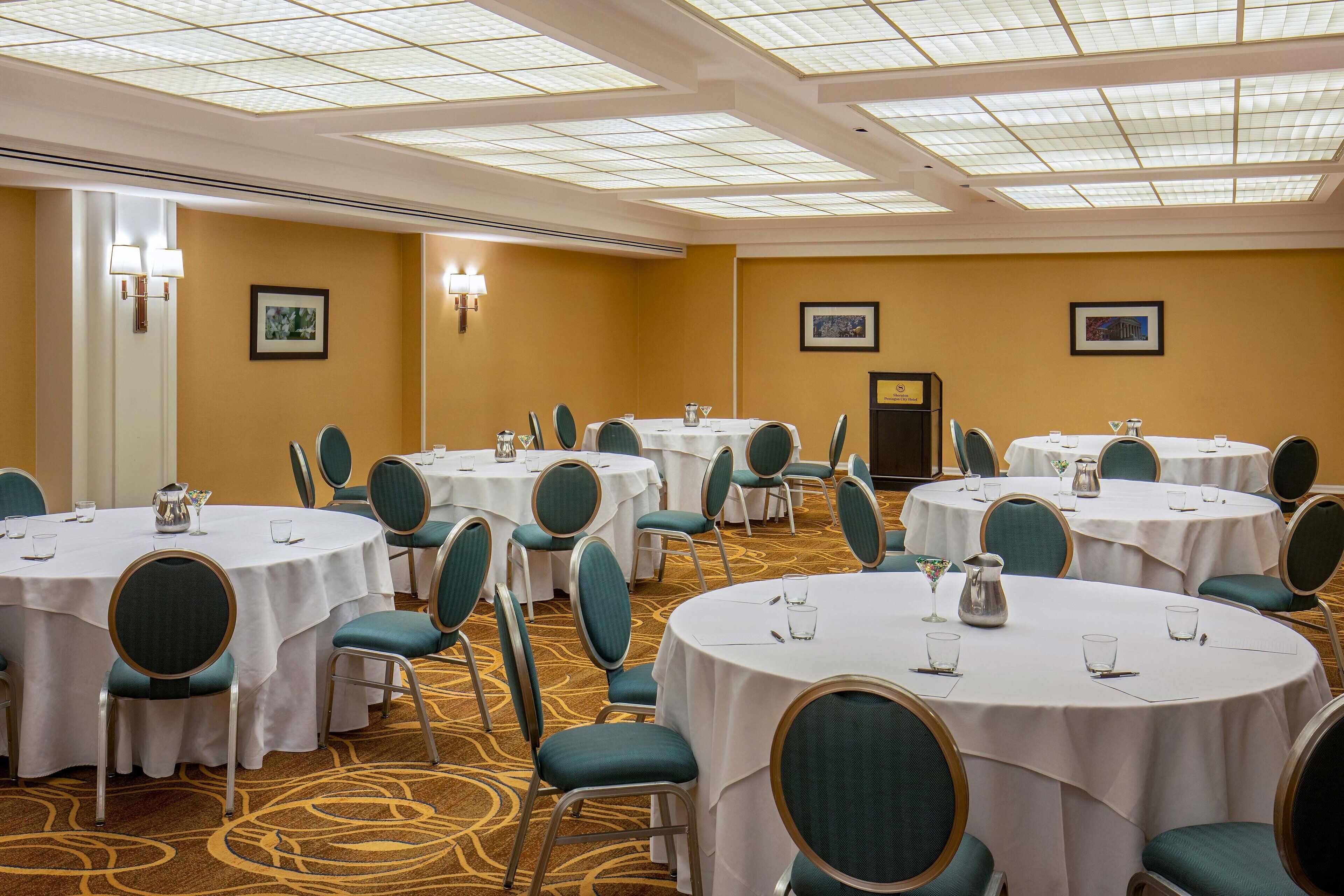 Un salón de conferencias con varias mesas redondas, sillas color turquesa y manteles blancos.