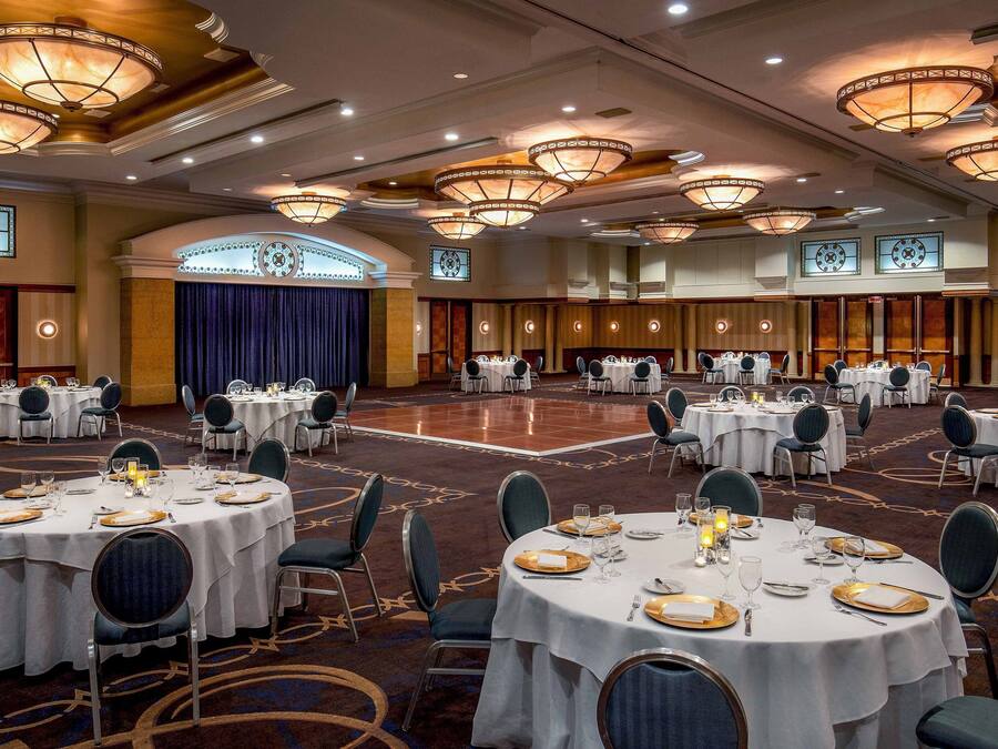 A banquet hall with round tables set for dining, featuring chandeliers and a carpeted floor.