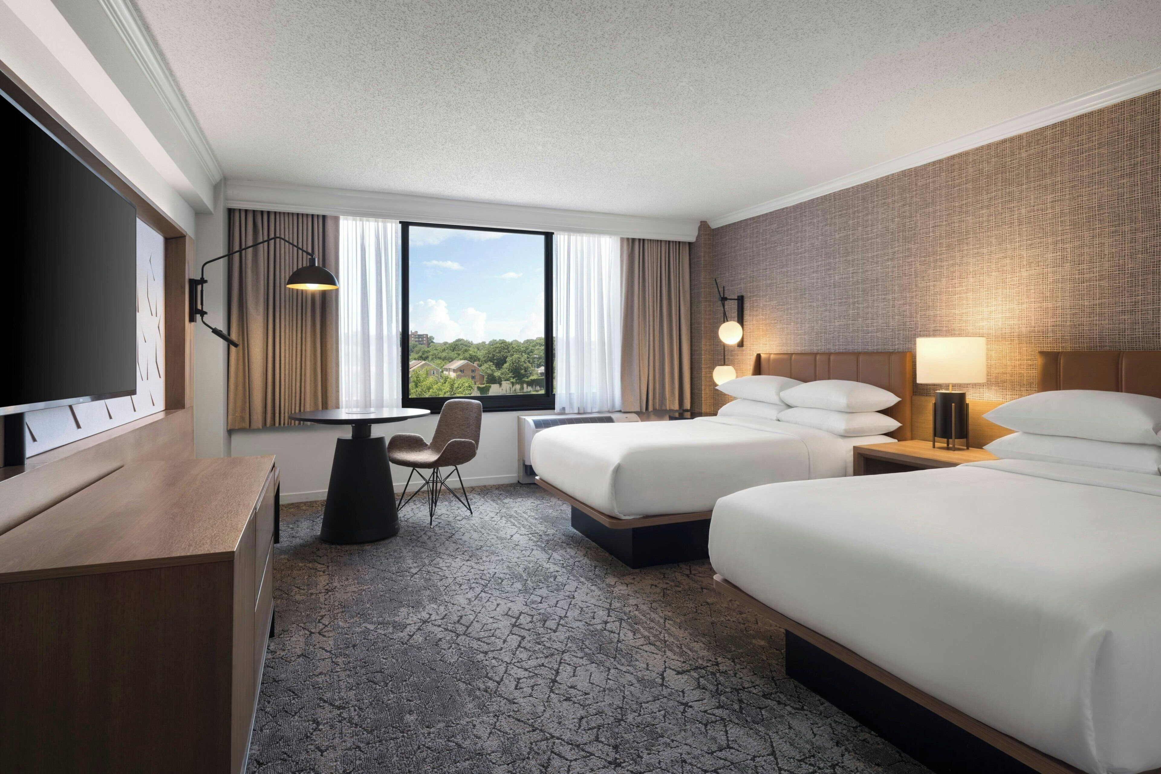 A hotel room with a bed, a desk, a chair, a TV, and a window with curtains.