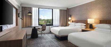 A hotel room with a bed, a desk, a chair, a TV, and a window with curtains.