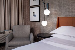 Una habitación de hotel con cama, una silla, una mesita y una lámpara fijada a la pared.