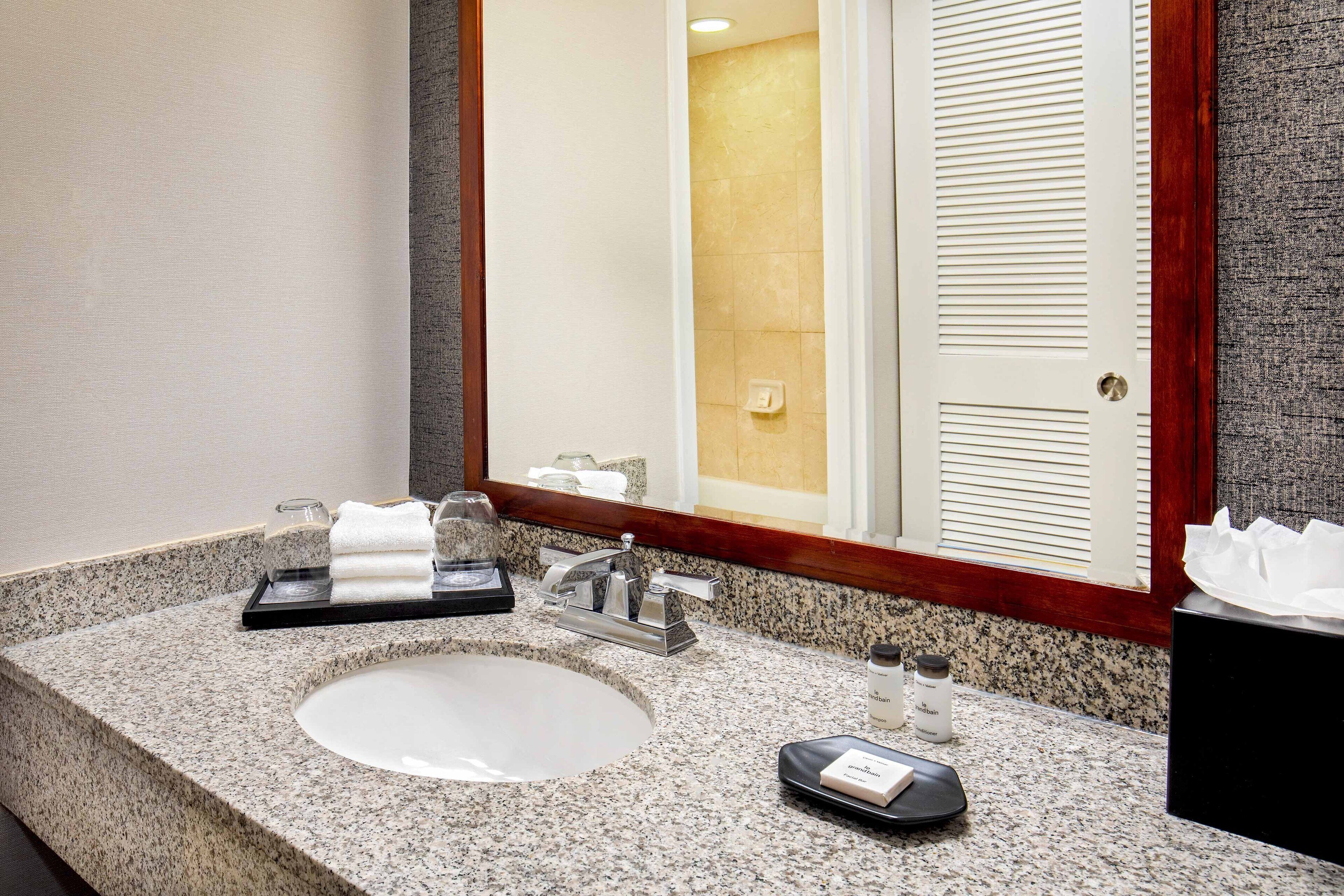 A bathroom with a granite countertop, two sinks, a mirror, and a towel rack.