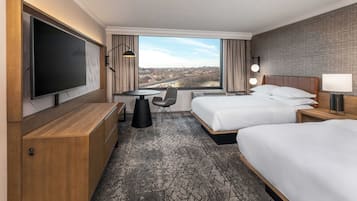 Habitación de hotel con dos camas, televisión, escritorio y un amplio ventanal con vistas a la ciudad.