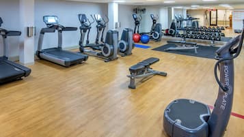 Un gimnasio con cintas de correr, elípticas, una banca y pesas sueltas.