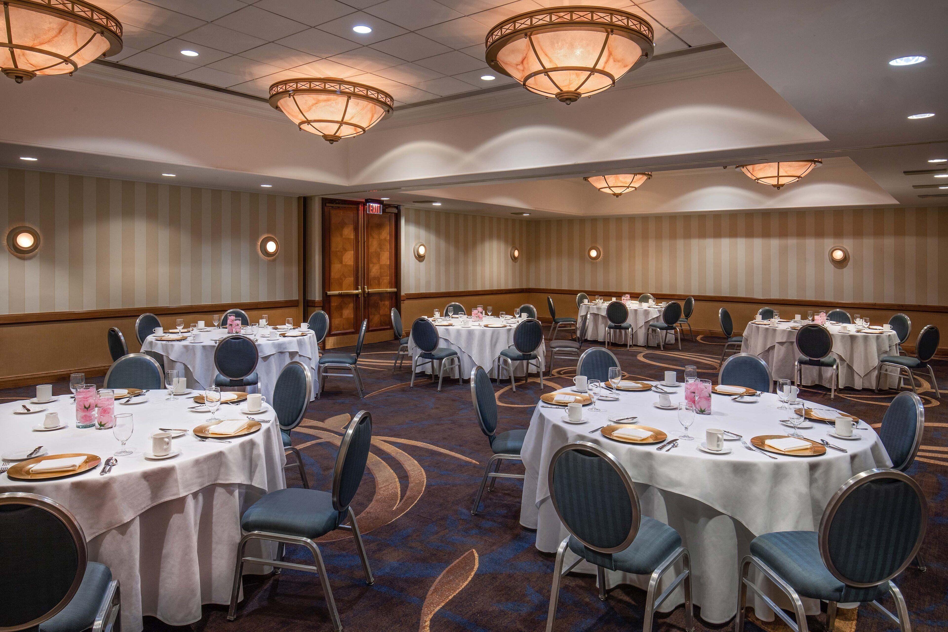 A banquet hall with round tables, chairs, and chandeliers.