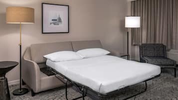 A hotel room with a bed, a chair, a floor lamp, a table, and a framed picture on the wall.
