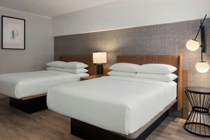 Habitación de hotel con dos camas, una mesita de noche, una lámpara y un aplique de pared.
