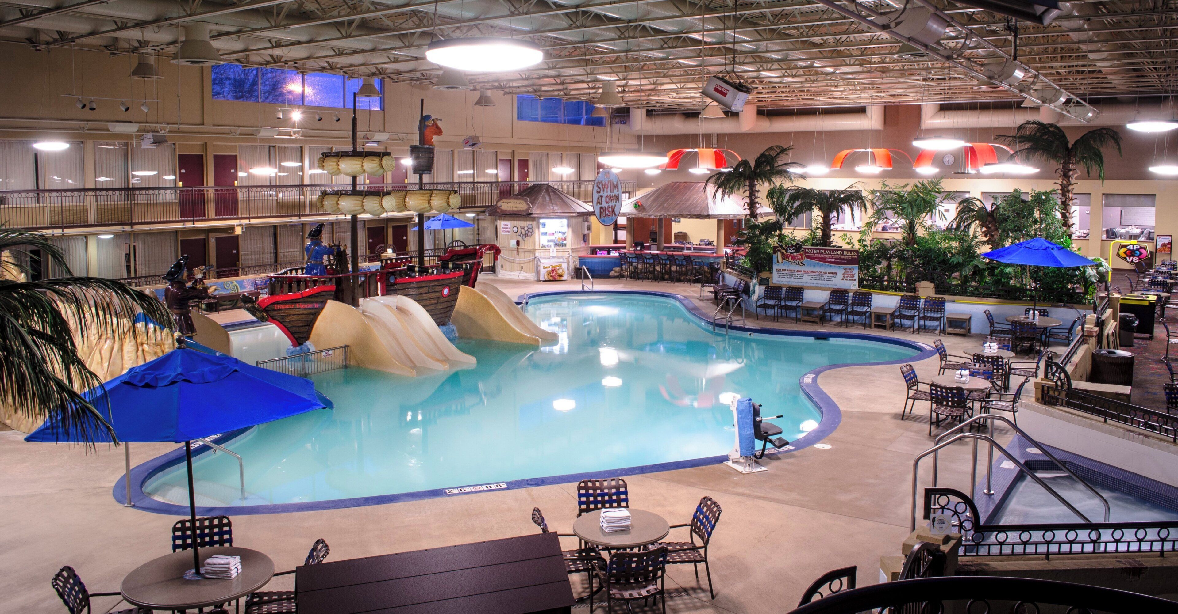An indoor swimming pool with slides, seating areas, and a bar.